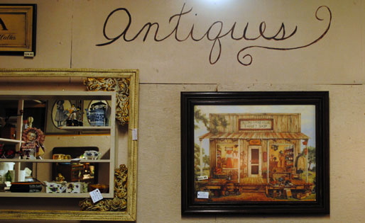 The word antiques is painted on the room wall above a photo of a general store and a gold framed mirror.