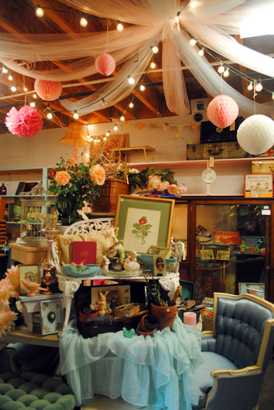 The photo features a decorated booth with hanging paper balls from the ceiling and an organized table with various items piled on top.